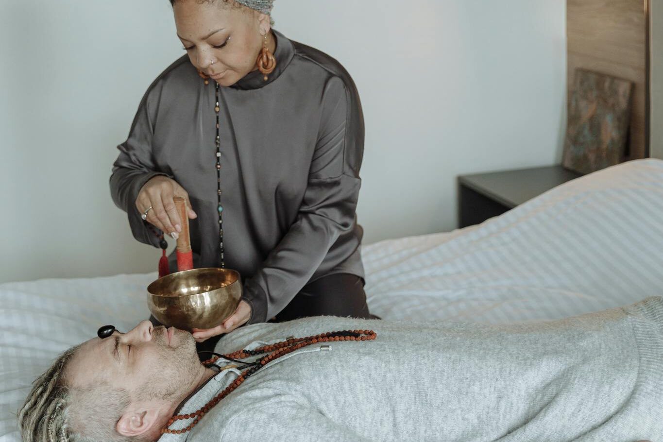 A woman performs a sound therapy session using a singing bowl on a resting person.
